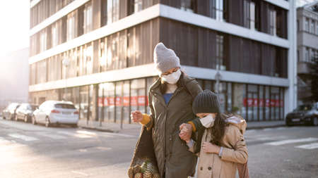 Mother with small daughter with shopping bags outdoors on street, coronavirus concept.の写真素材