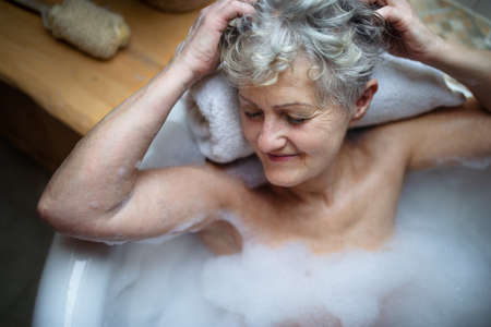 Top view of contented senior woman lying in bath tub at home, eyes closed.の写真素材
