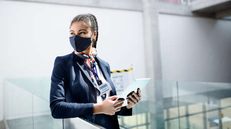 Young air hostess with tablet in airport lounge, travel and new normal.
