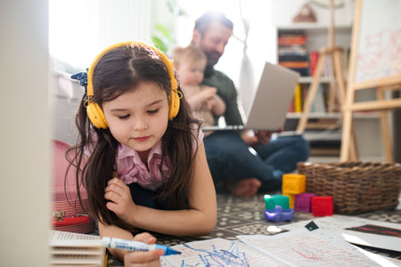 Father working with small daughters in bedroom, home office and distance learning concept.