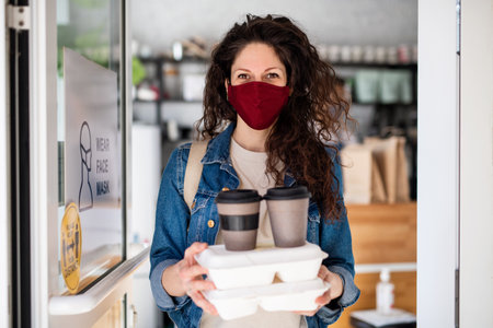 Woman with packed take away food and coffee, looking at camera. Coronavirus concept.の写真素材