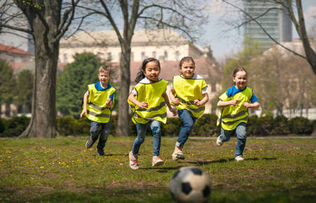 Small children playing football outdoors in city park, learning group education concept.の写真素材