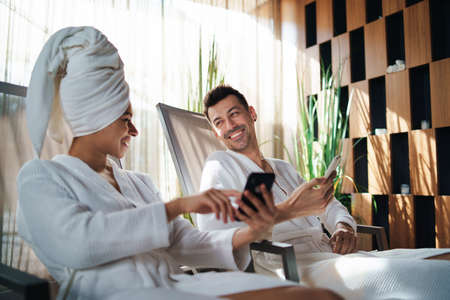 Portrait of young couple relaxing in spa resort, using smartphone.