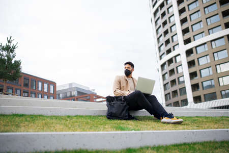 Man with laptop working outdoors in park in city