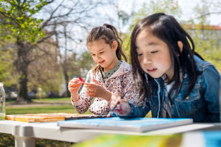 Small children painting pictures outdoors in city park, learning group education concept.の写真素材