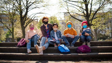 Teacher with small children sitting outdoors in city park, learning group education and virus concept.の写真素材