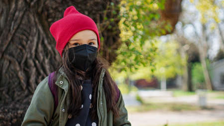 Portrait of small child with school bag standing outdoors on the way to school, looking at camera.の写真素材