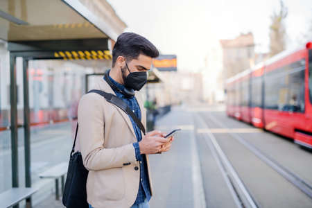 Young business man commuter with smartphone on the way to work outdoors in city