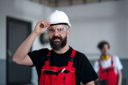 Portrait of worker with helmet and protective glasses indoors in factory looking at camera.の写真素材
