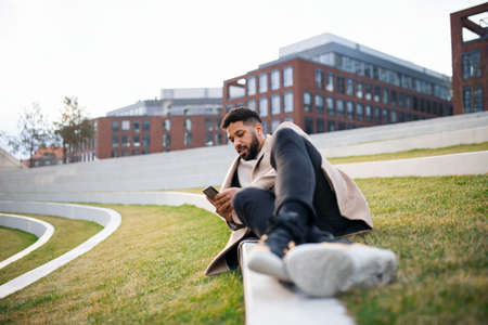 Man with smartphone working outdoors in park in city, resting in park.の写真素材