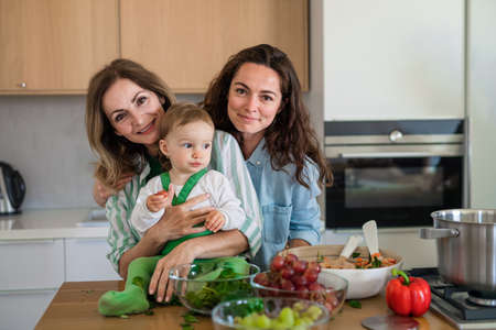 Mature mother with daughter and granddaughter indoors at home looking at camera when cooking.の写真素材