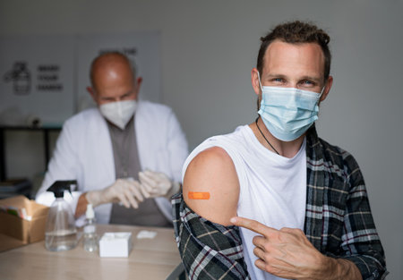 Happy mid adult man after covid-9 vaccination, pointing to plaster on arm and looking at camera.の写真素材