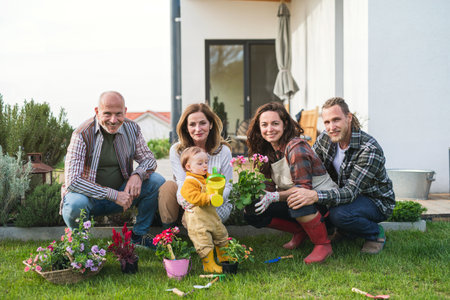 Happy multigeneration family outdoors planting flowers in garden at home, gardening concept.の写真素材
