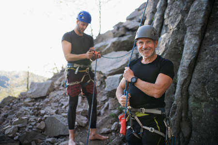 Senior man with instructor climbing rocks outdoors in nature, active lifestyle.
