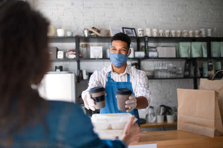 Waiter giving packed take away food and coffee to customer in coffee shop, coronavirus concept.の写真素材