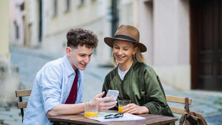 Young couple travelers using smartphone in city on holiday, sitting in outdoor cafe.の写真素材