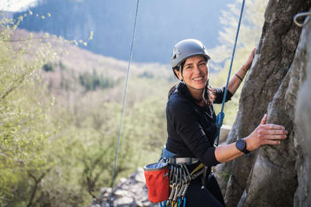 Senior woman climbing rocks and looking at camera outdoors in nature, active lifestyle.の写真素材