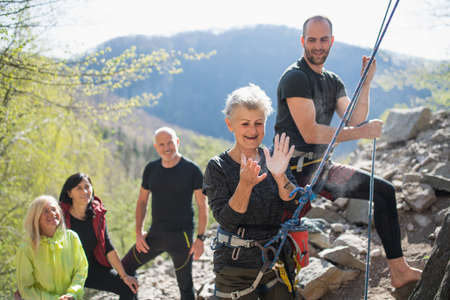 Group of seniors with instructor using chalk before climbing rocks outdoors in nature, active...