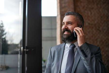 Portrait of young businessman standing indoors, using smartphone.