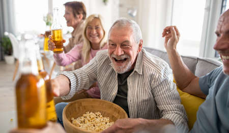 Group of senior friends watching movie indoors, party, social gathering and having fun concept.
