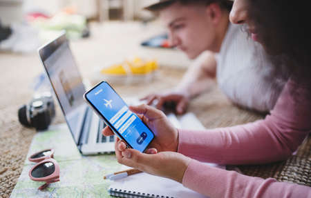 Unrecognizable couple with smartphone planning holiday, booking flight.