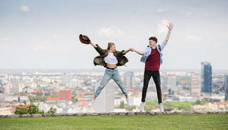 Cheerful young couple travelers in city on holiday, jumping. Cityscape in the background.の写真素材
