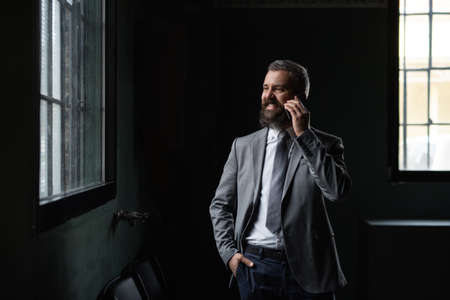 Portrait of mature businessman standing indoors, using smartphone.