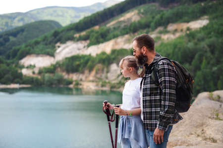 Happy preteen girl with father on hiking trip on summer holiday, looking at lake scenery.の写真素材