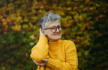 Senior woman standing outdoors against colorful natural autumn background, resting.