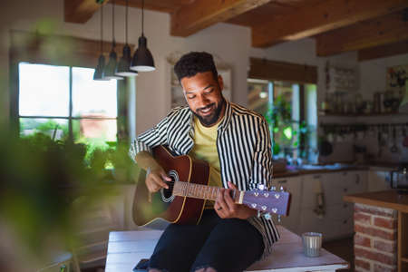 Happy young man with guitar indoors at home, relaxing.