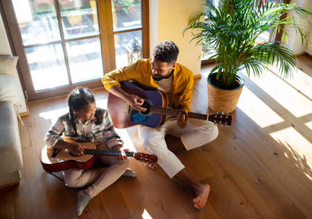 High-angle view of happy father with small daughter indoors at home, playing guitar.の写真素材