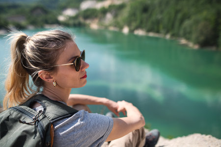 Mid adult woman tourist on hiking trip on summer holiday, resting by lake.の写真素材
