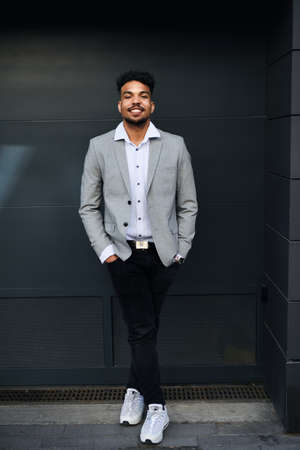 Portrait of young man student standing outdoors in city against black background, looking at camera.