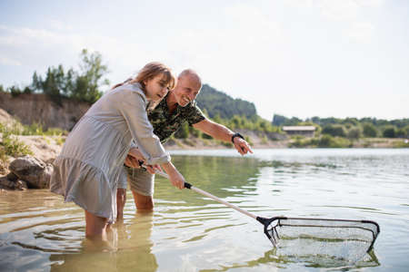 Happy preteen girl and grandfather with fishing net on summer holiday by lake.の写真素材