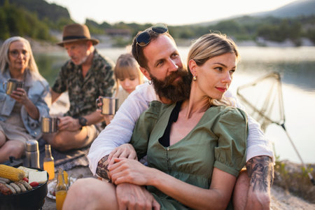Happy multigeneration family on summer holiday trip, barbecue by lake.