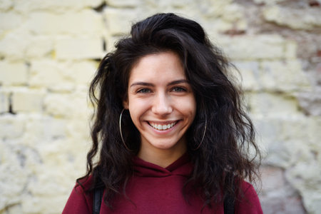 Portrait of young woman standing outdoors against stone background, looking at camera.