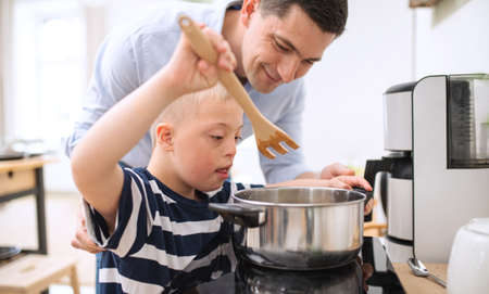 Father with happy down syndrome son indoors in kitchen, cooking.の写真素材