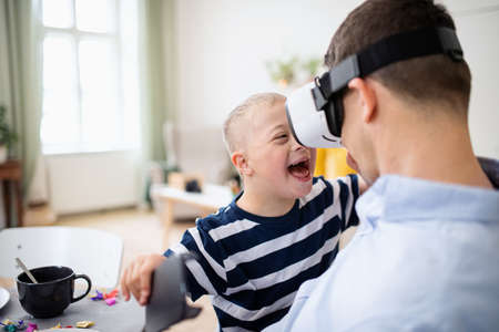 Father with happy down syndrome son indoors at home, using vr goggles.の写真素材