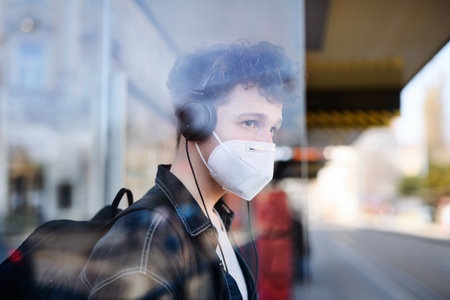 Portrait of young man commuter standing on bus stop outdoors in city, coronavirus concept.の写真素材