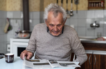 Portrait of elderly man sitting at the table indoors at home, reading newspapers.の写真素材