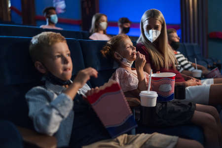 Mother with happy small children watching film in the cinema, coronavirus concept.