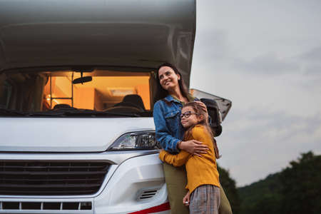 Mother with daughter standing by car outdoors in campsite at dusk, caravan family holiday trip.の写真素材