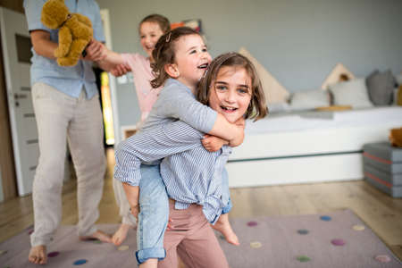 Unrecognizable father with three daughters indoors at home, playing and having fun.の写真素材