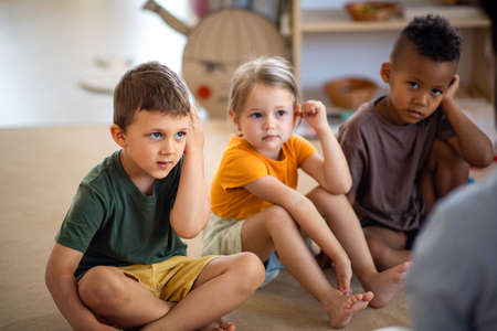 Group of small nursery school children sitting on floor indoors in classroom, listening to teacher.の写真素材