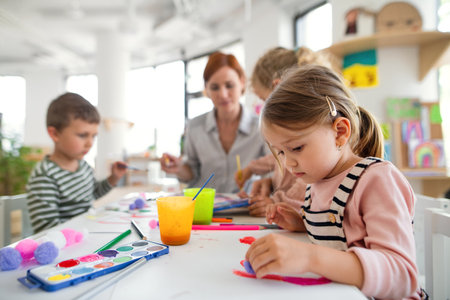 Group of small nursery school children with teacher indoors in classroom, painting.の写真素材
