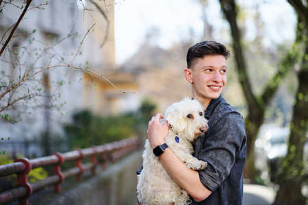 Portrait of young man walking outdoors on street in city, holding dog.