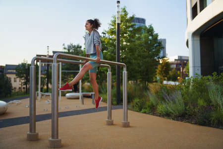 Mid adult woman doing exercise on parallel bars outdoors in city workout park, healthy lifestyle...