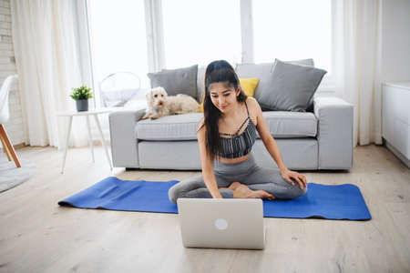 Portrait of young sport woman with laptop doing exercise indoors at home, healthy lifestyle concept.の写真素材