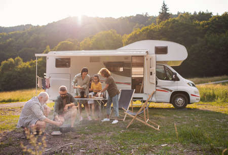 Multi-generation family sitting and eating outdoors by car, caravan holiday trip.の写真素材