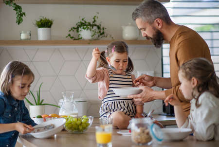 Father with three daughters indoors at home, eating breakfast in kitchen.の写真素材